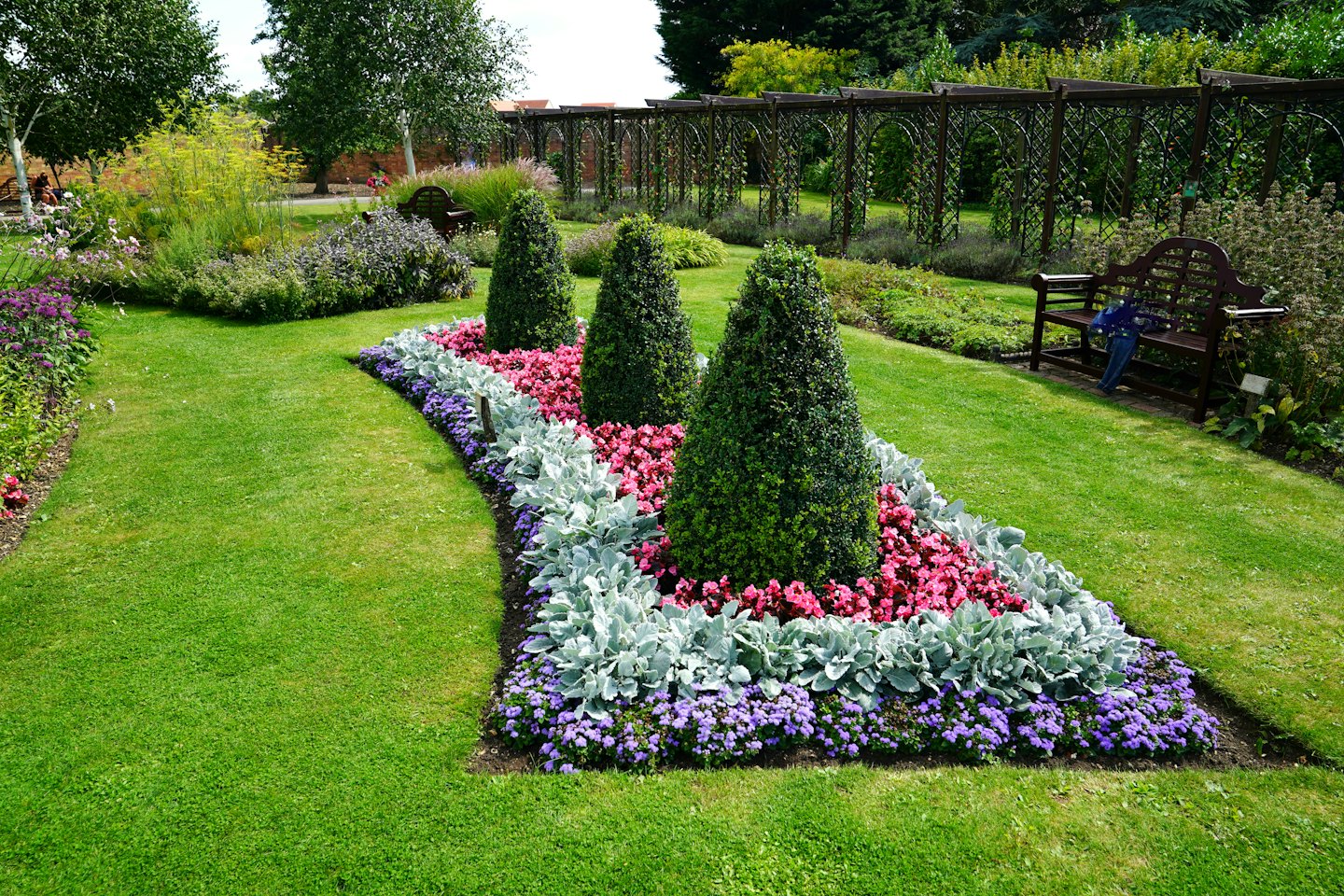 Ein Gartenweg, gesäumt von blühenden Pflanzen und grünen Formschnittgehölzen.